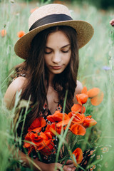 Beautiful young free girl in a hat in a summer field of red poppies with a bouquet. Soft selective focus.