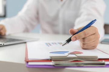 businessman in white shirt working and calculating about finance with graph chart, document report and laptop computer on desk at home, work from home, marketing and financial business concept