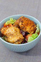 Chicken breast in a bowl with tomato, lettuce, onion, cucumber, and pepper in a vinaigrette.  On a grey marl tablecloth