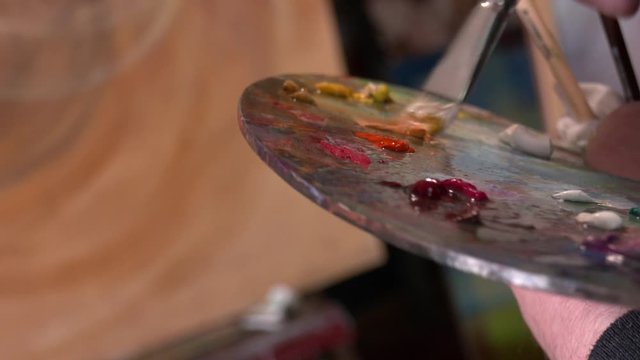 artist brush mix color oil painting on palette is holding in his hand closeup. Brush in hand. Oil painting. Beatiful picture. Palette paint.
