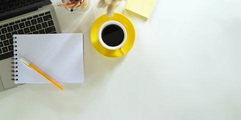 Top view image of computer laptop putting on white working desk that surrounded by note, pen, coffee cup, post it, pencil holder and wild grass. Orderly workspace concept.