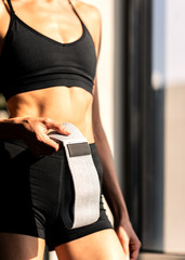 Intense work. Cropped shot of a sporty woman in black sportswear holding rubber resistance band while going to exercise with it at home. Workout, body goals concept. Vertical shot