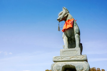 Fox statue of Fushimi Inari Shrine on blue sky background. In Japanese folk legend story that the fox represents the Inari god come to the human world give to exuberance.