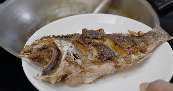 Ladling fried fish with chili sauce into plate, follow focus, Thai traditional food

