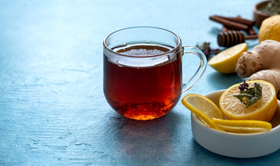 Ginger tea with lemon in glass cup at blue background. Space for a text.