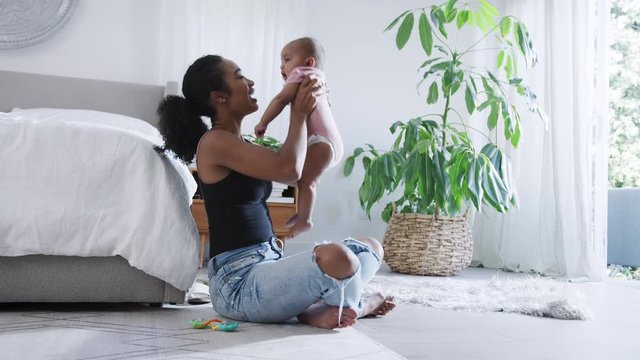 Loving Mother Playing With Baby Daughter Sitting On Floor In Bedroom
