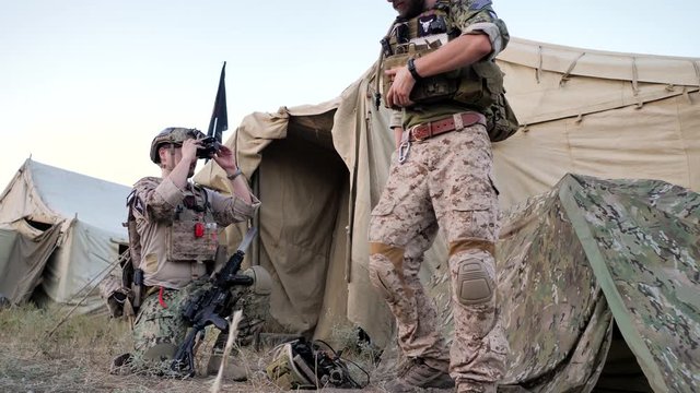 One soldier sets up the night-vision device, the other wears a bulletproof vest