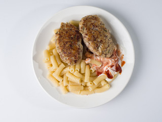 Meat cutlets with a side dish of penne rigate in a white round plate. Top view