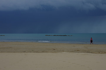 A woman walks on the deserted beach, in the background there is a storm.