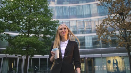 From below of serious blond executive woman in suit having coffee in paper cup looking away on street.