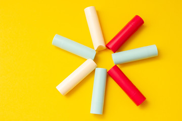Obraz premium Bright multi-colored cosmetic lipstick on a yellow background in the shape of the sun