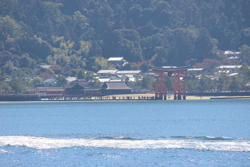 Looking at Miyajima island from the ferry. Floating red giant Grand O-Torii gate stands in bay beach at low tide on sunny day, Hiroshima City, Hiroshima Prefecture, Japan. 厳島神社