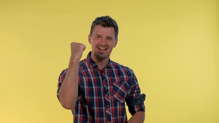 Excited young man yelling and raising fists in cheer on yellow background. He supporting and encouraging somebody.