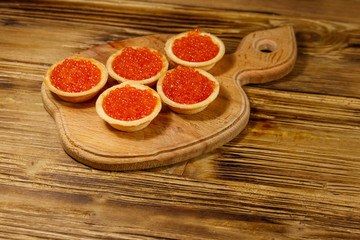 Tartlets with red caviar on a wooden table