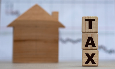 TAX word on cubes on the background of a wooden house and graphics