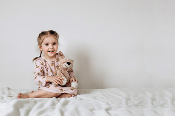 Little three year old girl plays and hugs a toy cat on a white background
