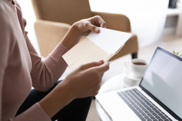 Close up side view young woman holding craft paper envelope correspondence, getting blank paper sheet invitation. Worrying student received university admission notification with postal letter.