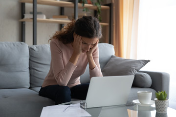 Stressed overworked young female student looking at laptop monitor, suffering from headache....