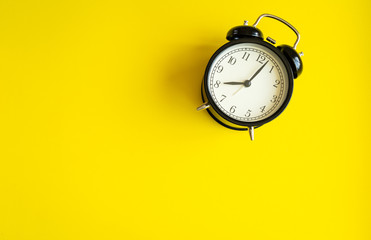 black alarm clock from 7 a.m. to 8 a.m. with bright yellow  background and shadows from the changing light of the sun's movements in morning and working hours concept front shot.