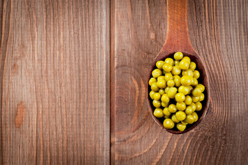 Canned green peas in a wooden spoon lying on a wooden surface of the table.