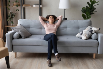 Front full length view tranquil millennial pretty woman relaxing on comfortable sofa in living...