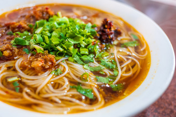 spicy chinese noodle with pork and vegetable in white bowl