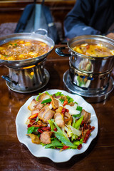 Spicy yak meat in hotpot and fried pig in white plate on wooden table