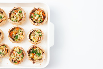 Caps of champignon mushrooms stuffed with vegetables on a white plate. Cooking process. Prepared for baking. Top view.