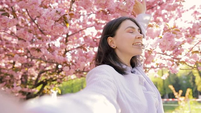 Beautiful woman having video chat using smartphone outdoors sharing travel adventure friends showing sakura blossom. Girl filming selfie video photo for social media. Japan vacation slow motion