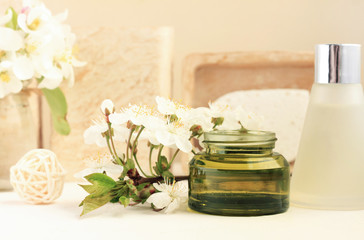 Botanical spa treatment, green glass cosmetic jar, essential oil, apple blossom, beige soft tones backgorund. Herbal aromatherapy beauty product. 
