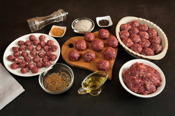 Raw homemade beef meatballs, minced meat, olive oil, salt and spices are close-up ready to cook on a dark concrete background in the kitchen. Selective focus.