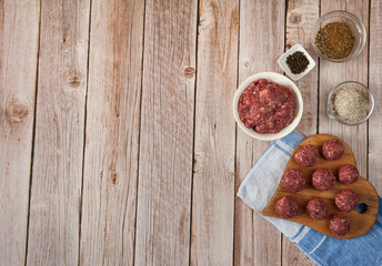 Fototapeta na wymiar Raw homemade beef meatballs, minced meat, salt and spices are ready to cook on a wooden background in the kitchen. Free space.