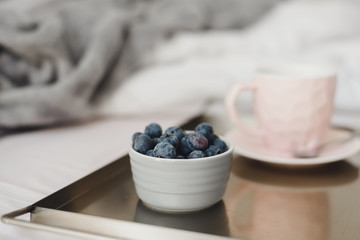 Blueberries for breakfast served in bed with a cup of coffee of pink color on metal tray. Healthy dessert. Breakfast in bed