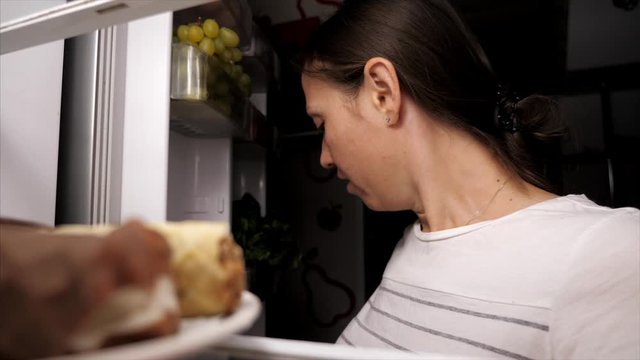 Adult Female Is Opening Fridge With Yawn At Night And Looking At Sweet Eclair. Woman Is Resisting Temptation To Eat Dessert And Closing Door While Being On Diet