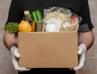 Coronavirus volunteer, food donation. Food in a box, in hands with gloves, close-up. Food delivery.