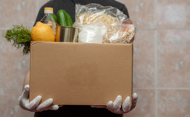Coronavirus volunteer, food donation. Food in a box, in hands with gloves, close-up. Food delivery.