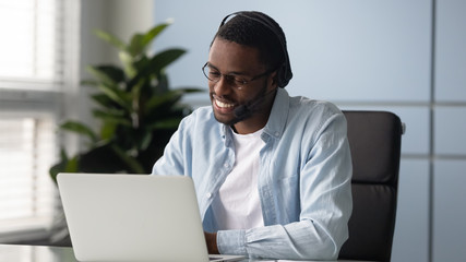 African american businessman talking using headphones looking at laptop screen. Happy smiling man operator working in call center and support people. Manager communicating with client.