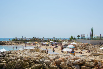People on the beach, having fun next to luxury hotel on the coastline, pool, umbrellas and beach chairs