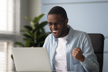 African american businessman with glasses celebrating business success achievement, shouting. Diverse employee feeling motivated by good work looking at laptop screen, receive great news in email.