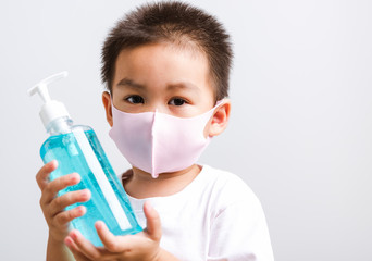 Closeup portrait Asian little child boy holding show bottle pump dispenser sanitizer alcohol gel hand wash cleaning, COVID-19 or coronavirus protection concept, isolated on white background