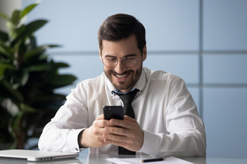 Obraz na płótnie Canvas Happy businessman glad to good news message on smartphone. Smiling man employee fun using online chat on modern cell phone. Male customer satisfied with quality by service.