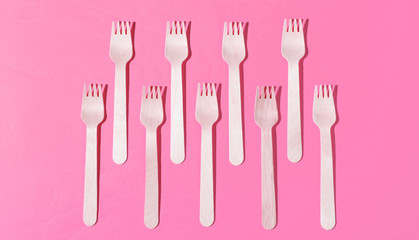 Many eco-friendly wooden forks on pink background. Minimalistic eco concept. Pop art
