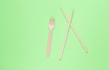 Eco cutlery. Chinese chopsticks, wooden fork on green background. Top view