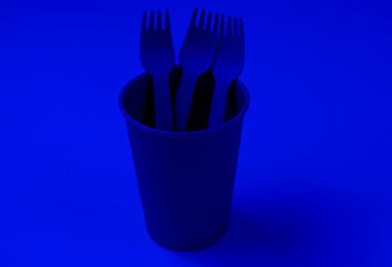 Disposable empty coffee cup with forks of natural materials. Blue neon light. Eco friendly concept. Top view