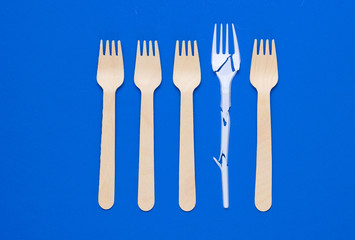 Minimalistic ecologically clean still life. Pop Art. Broken plastic fork among many wooden forks on blue background. Cutlery made from natural materials
