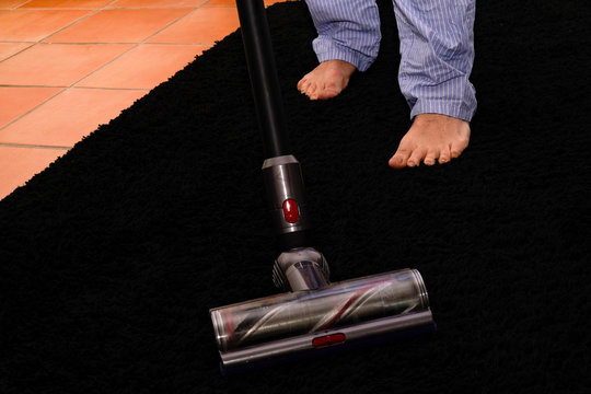 homme en pyjama passant l'aspirateur sans fil sur un tapis noir &eacute;pais &agrave; franche pendant le confinement