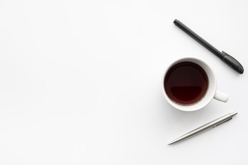 Cup of coffee with pens are on top of white office desk table. Top view with copy space, flat lay.