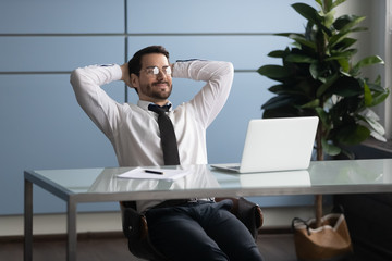 Smiling businessman with hands behind head relaxing in comfortable office. Happy successful employee stretching during break in office after work done, satisfied by good result