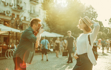 Young cheerful couple of hipsters are photographed on a retro camera while walking around the city. Male photographer photographs a stylishly dressed young woman