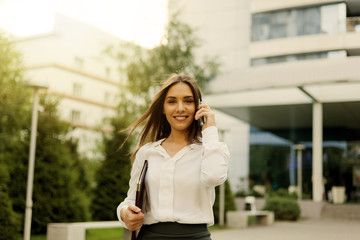 Businesswoman. Young attractive female manager wearing a skirt and a blouse talking on phone at background of the city landscape. All in business